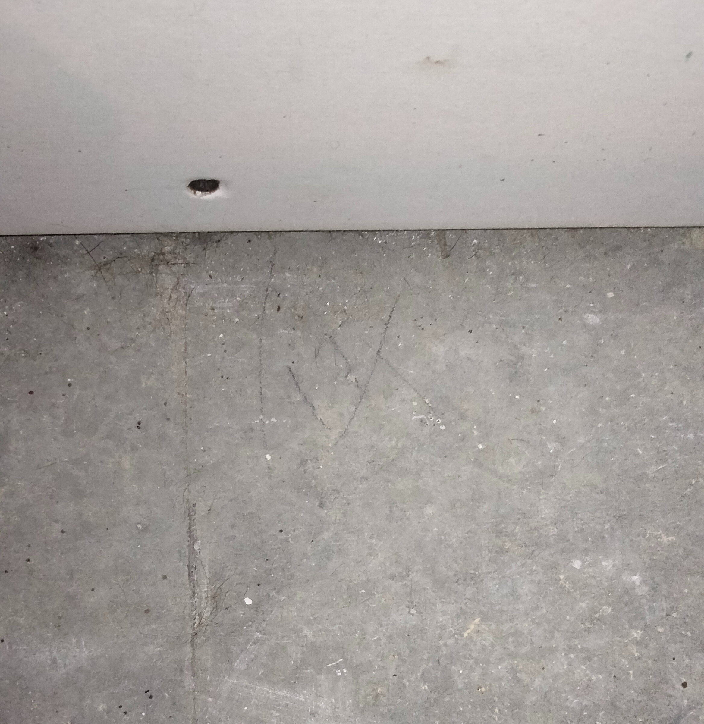 A concrete floor with a faint pencil marking. It has the number 17 along with a vertical line on the left, in line with a screw on the wall.
