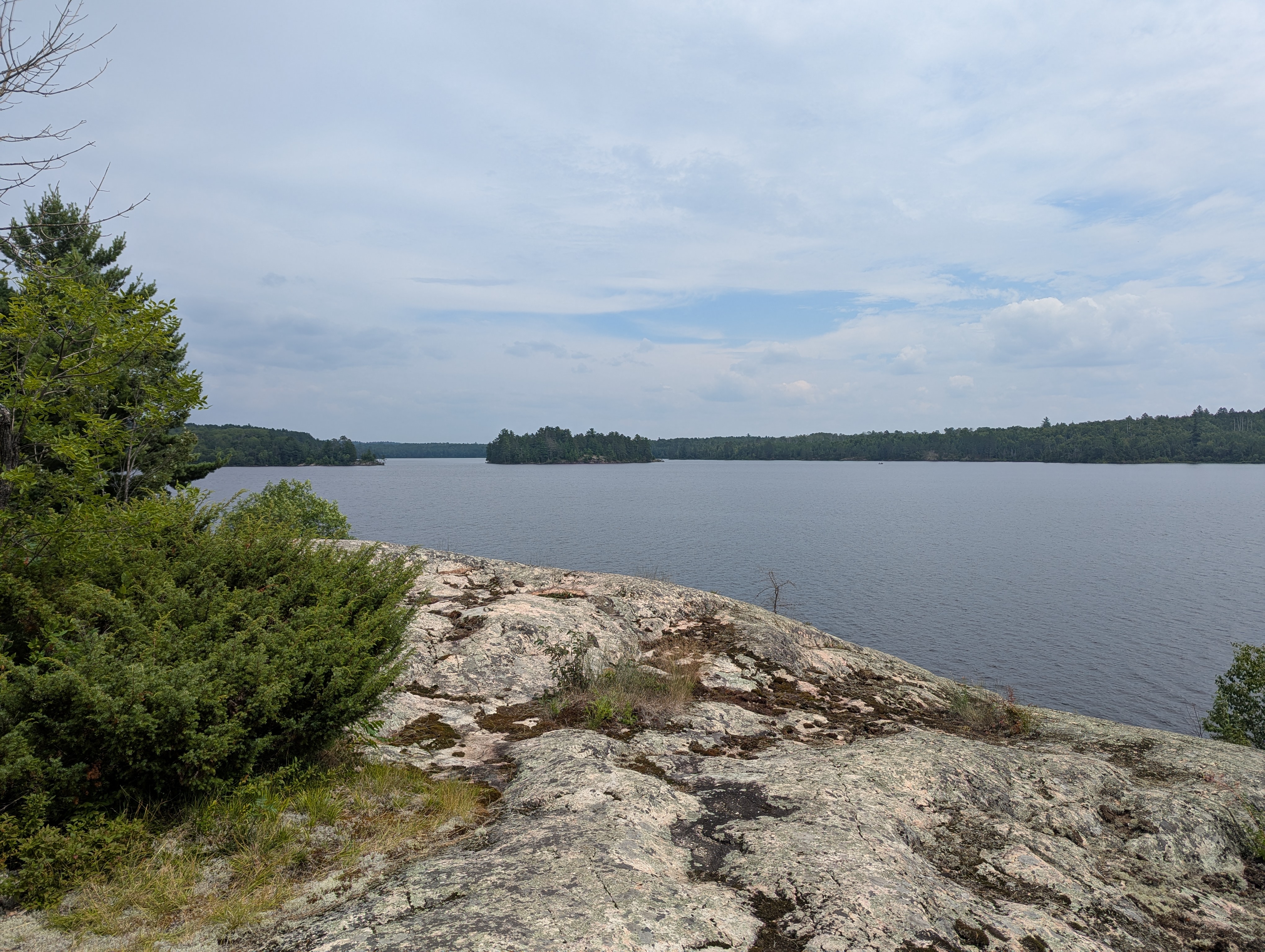 A photograph on a high granite rock above a lake. An island is visible on the lake in the distance.