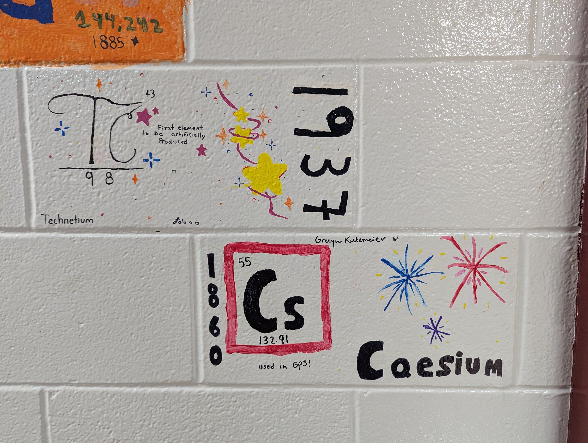 Two painted cinderblocks. Technetium is on one and says that it was the first syntheically produced atom. Caesium is on the other and features fireworks because it used to color different shells.