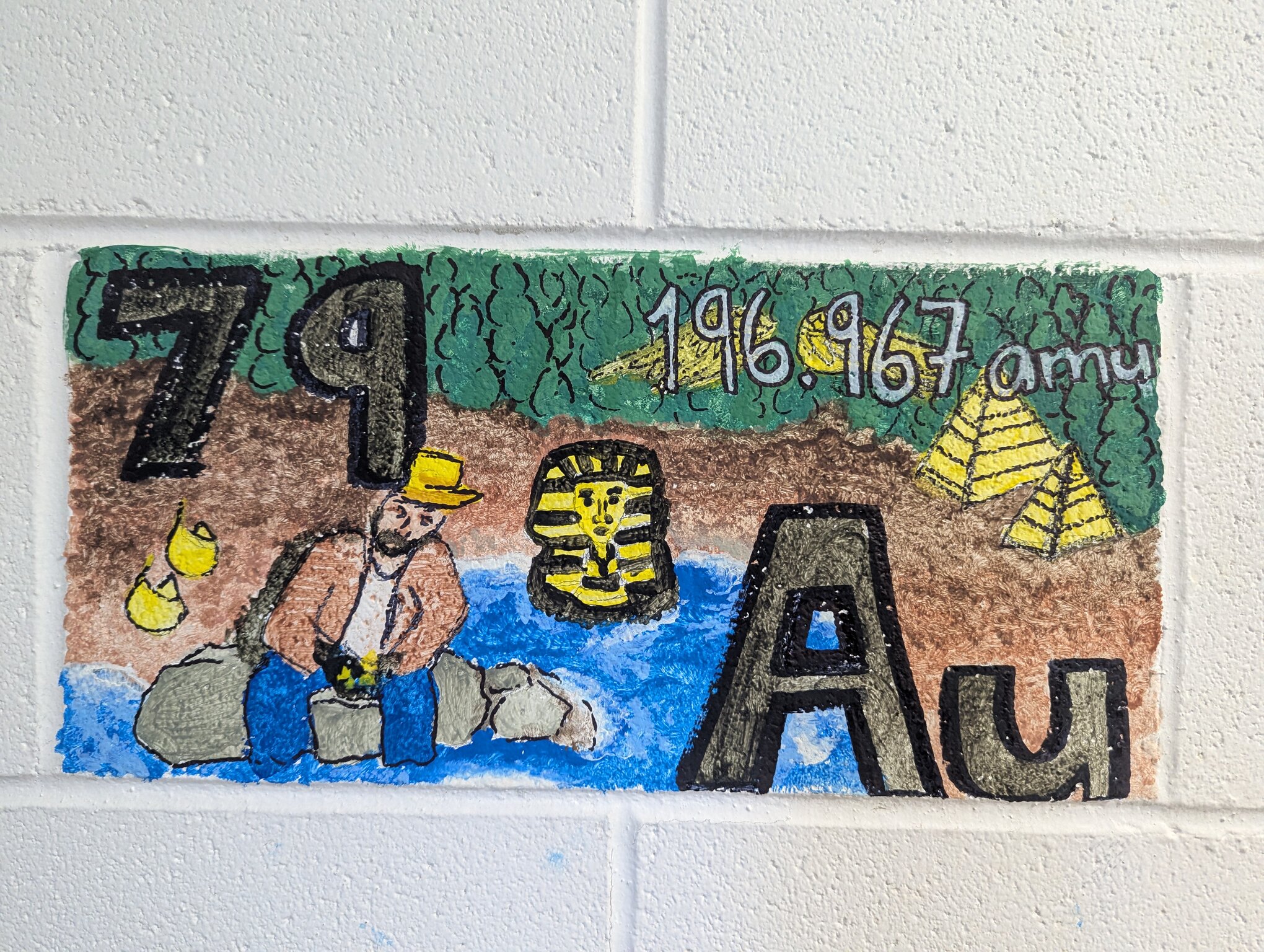 A painted cinderblock featuring gold. The symbol, Au, is paired with a miner from the gold rush and Egyptian symbolism because they used it so much.